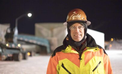 Andy wears a Carlile hard hat and bight orange and yellow heavy coat while posing for the camera.