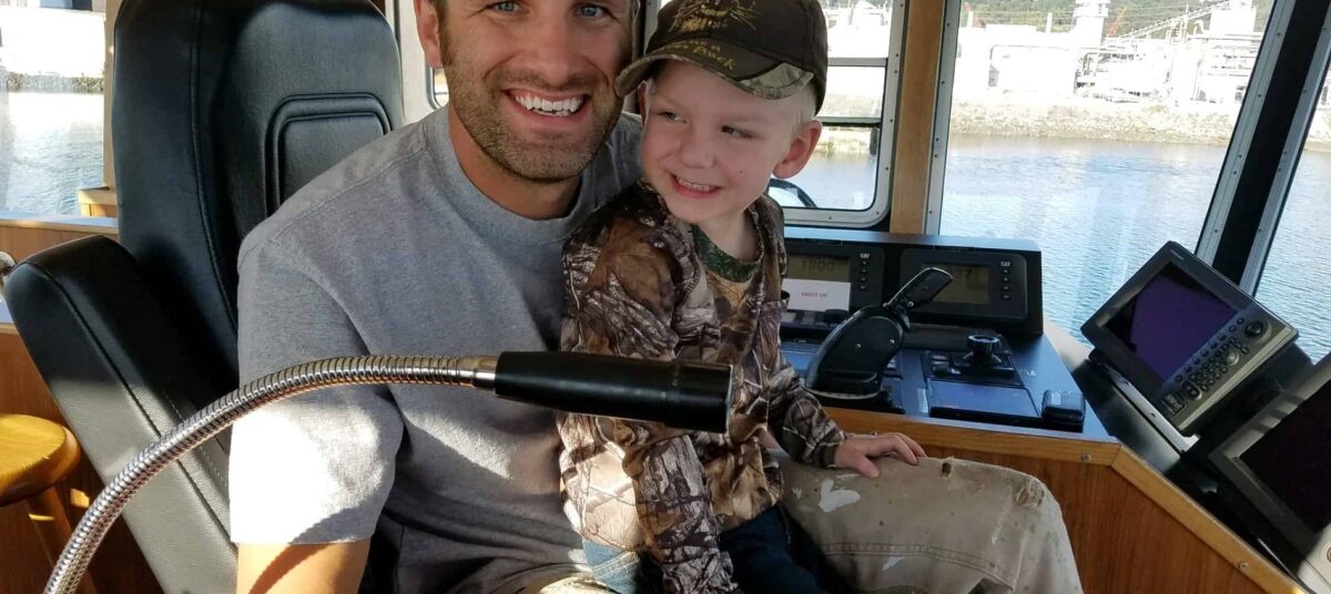 Andy holds his son in his lap at the helm of a Foss tug.
