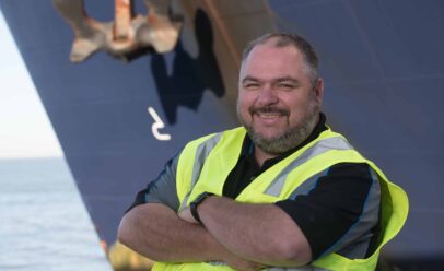 Godwin smiles with his arms crossed. Behind him, the bow of a docked ship.