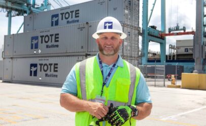 Bradley, removing his glove, smiles for the camera in a TOTE shipyard.