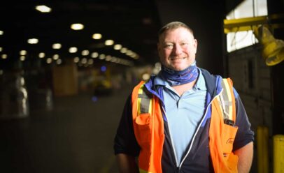 Kevin smiles in a warehouse, wearing orange
