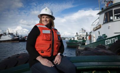 Erin poses in a white Foss hard hat, and orange life vest.