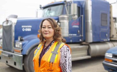 Lisa wears an orange Carlile reflective vest in front of a Carlile truck cab.