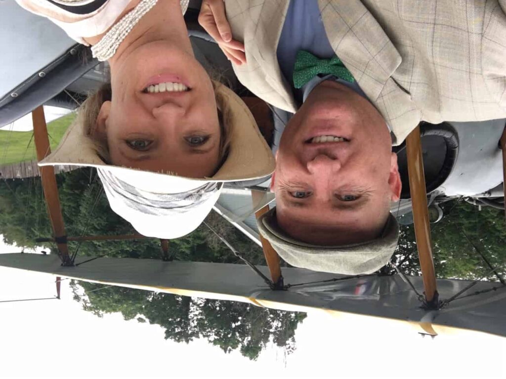 Adam poses with his wife in front of an old biplane.