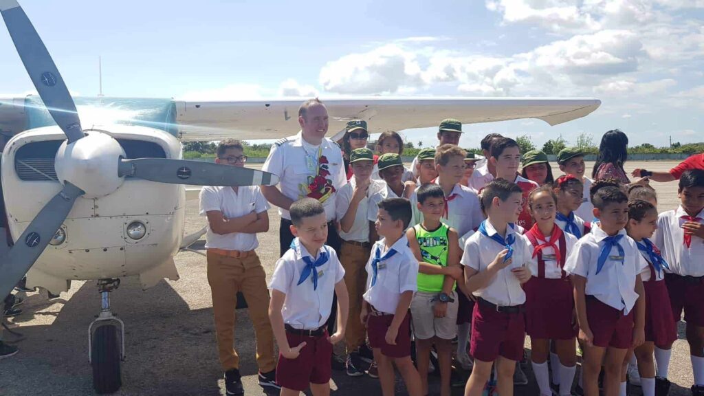 Adam in NAC uniform poses with kids in front of a Cessna airplane.
