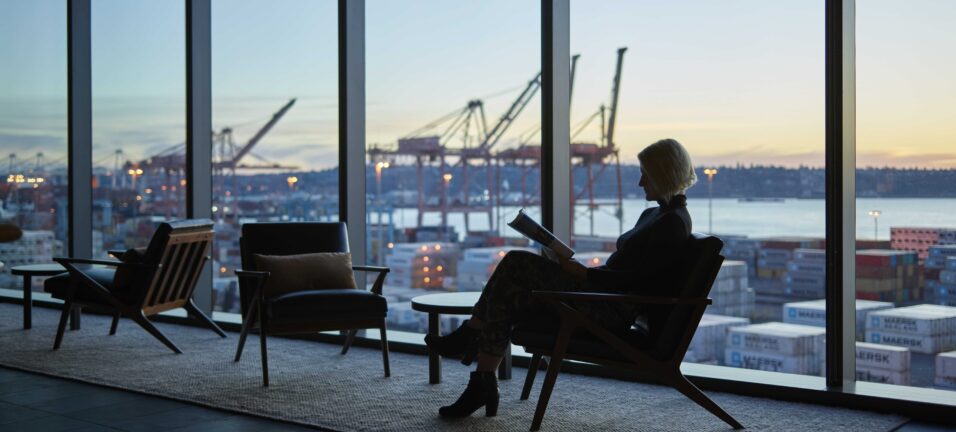woman reading in front of windows overlooking the Port of Seattle