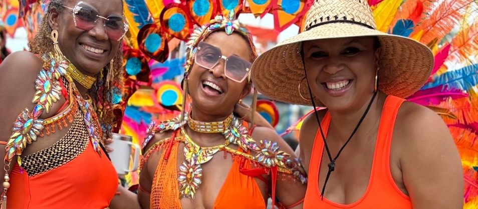 A photo of three smiling women in orange Carnival costumes